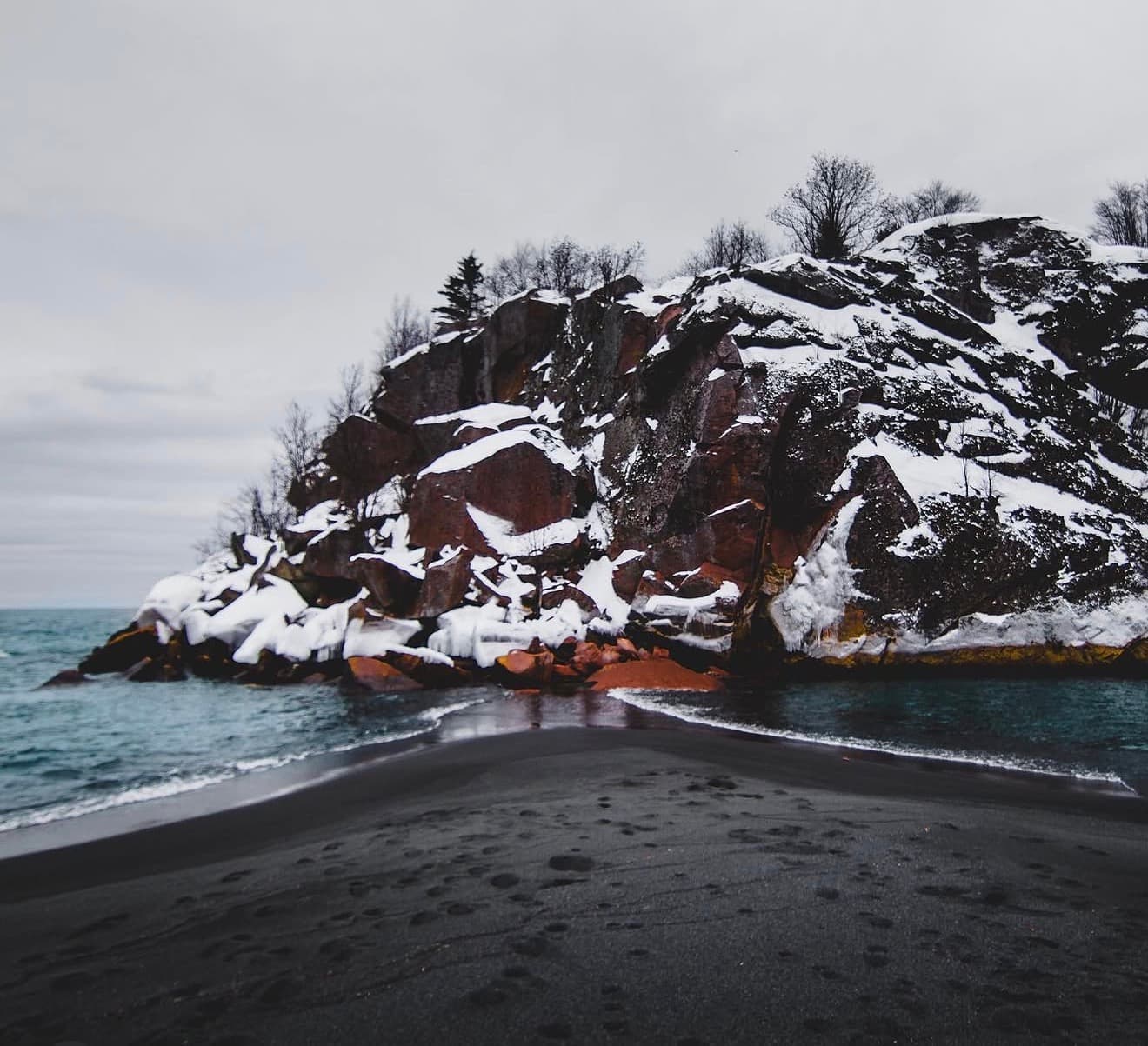 Snow-covered rock outcrop on a black sand beach along Lake Superior's North Shore, photographed by Easton