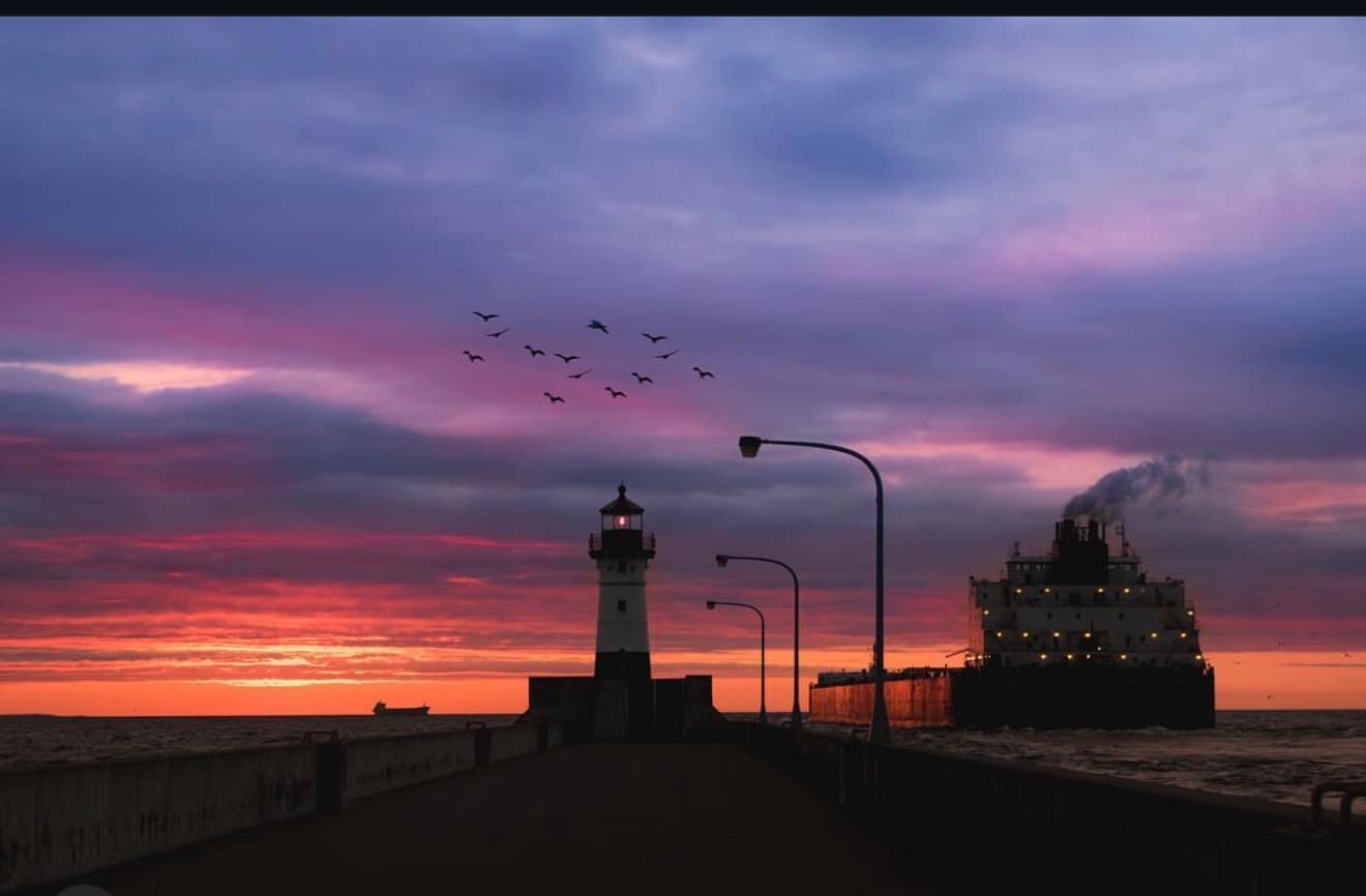 South Pier lighthouse at sunset with an ore boat and a flock of birds over Lake Superior in Duluth
