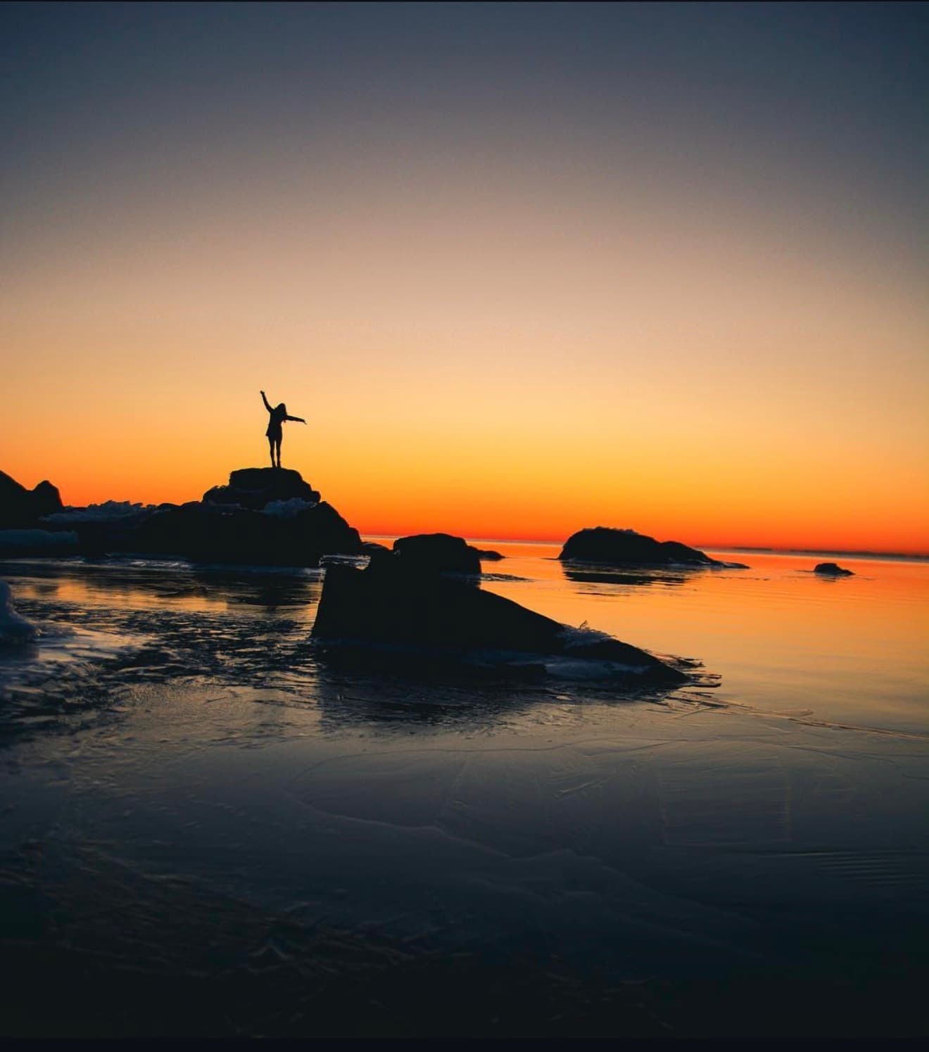 Silhouette of a person with arms raised on a rock at sunset over Lake Superior, a symbol of hope